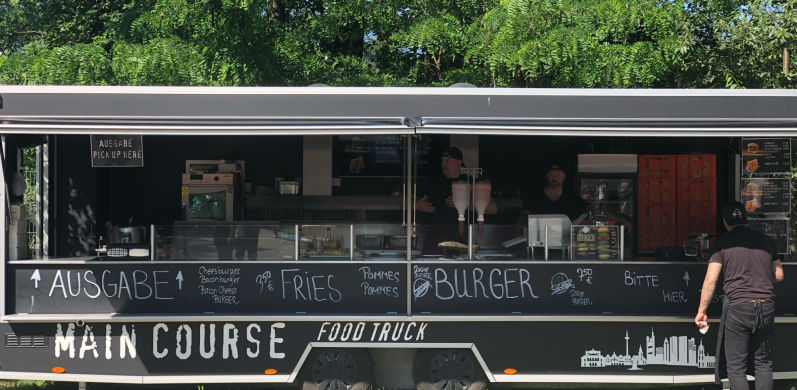 Ein Foodtruck mit Menütafel und einem Kunden, der das Angebot begutachtet.