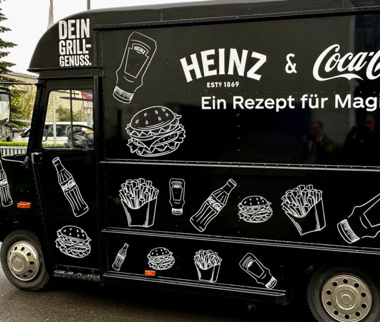 Schwarzer Foodtruck mit Heinz und Coca-Cola Werbung, besprüht mit Speisenmotiven.