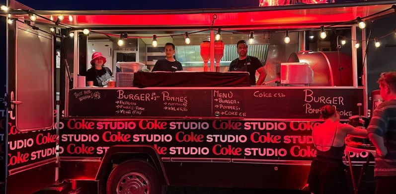 Drei Verkäufer in einem Food-Truck mit rotem Licht und Menü auf der Vorderseite.